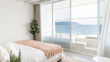 Un dormitorio con una cama grande, una planta en maceta y vistas al mar a través de una puerta corrediza de vidrio.