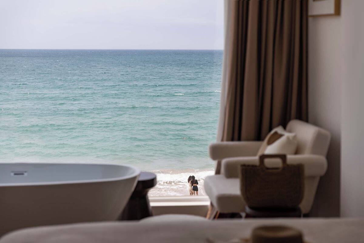 A room with a view of the ocean, a bathtub, a chair, and a handbag.