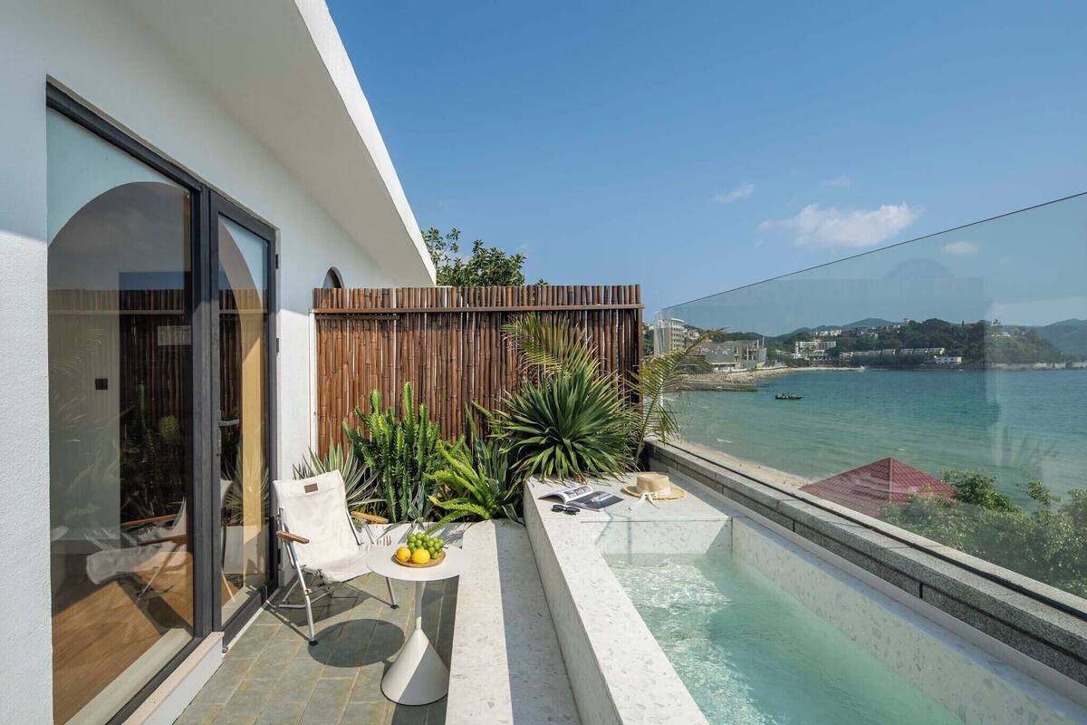 A balcony with a view of the sea, a wooden fence, and a table with fruits.