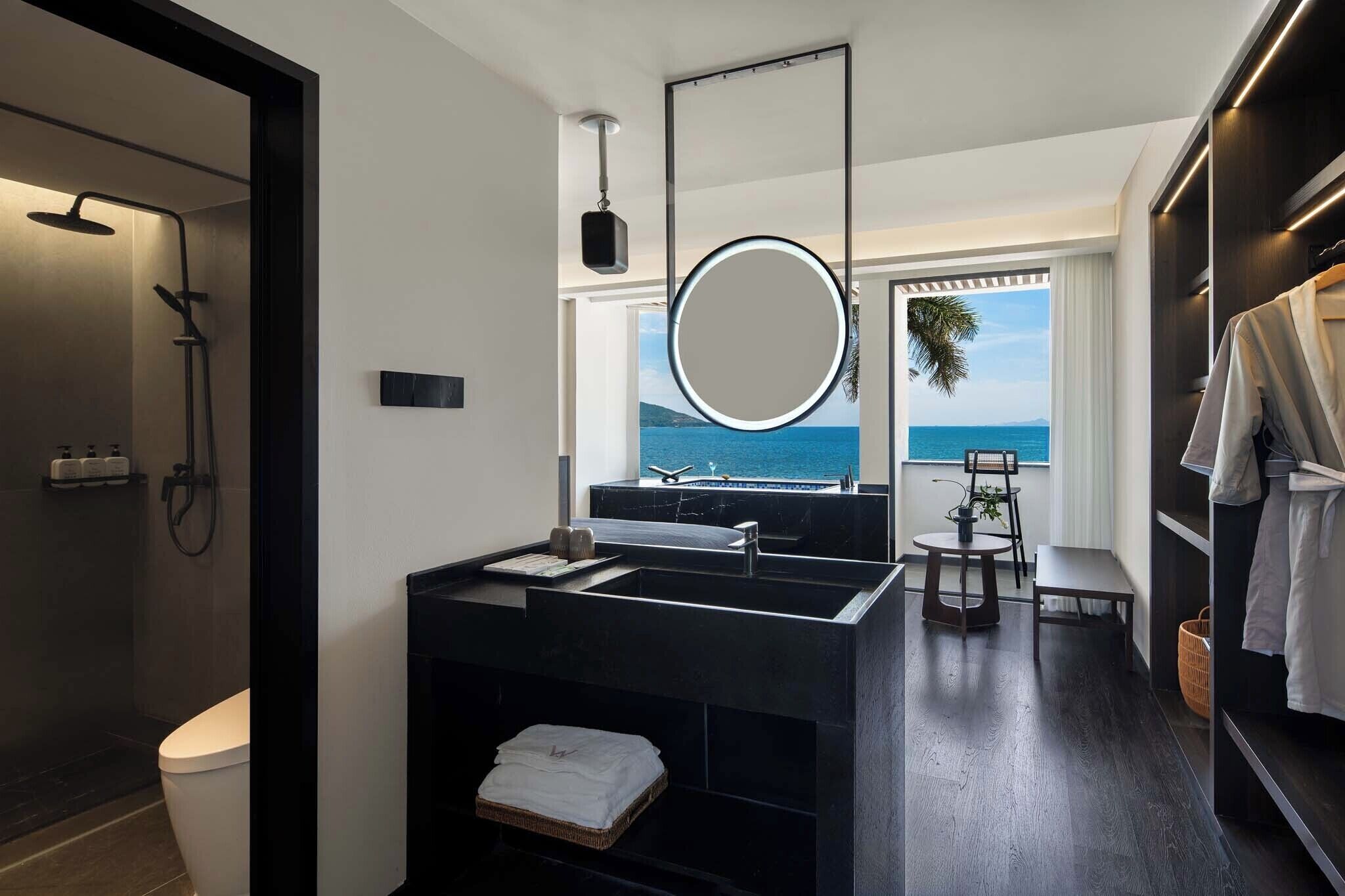 Un baño moderno con un tocador negro, un espejo grande y vistas al mar.