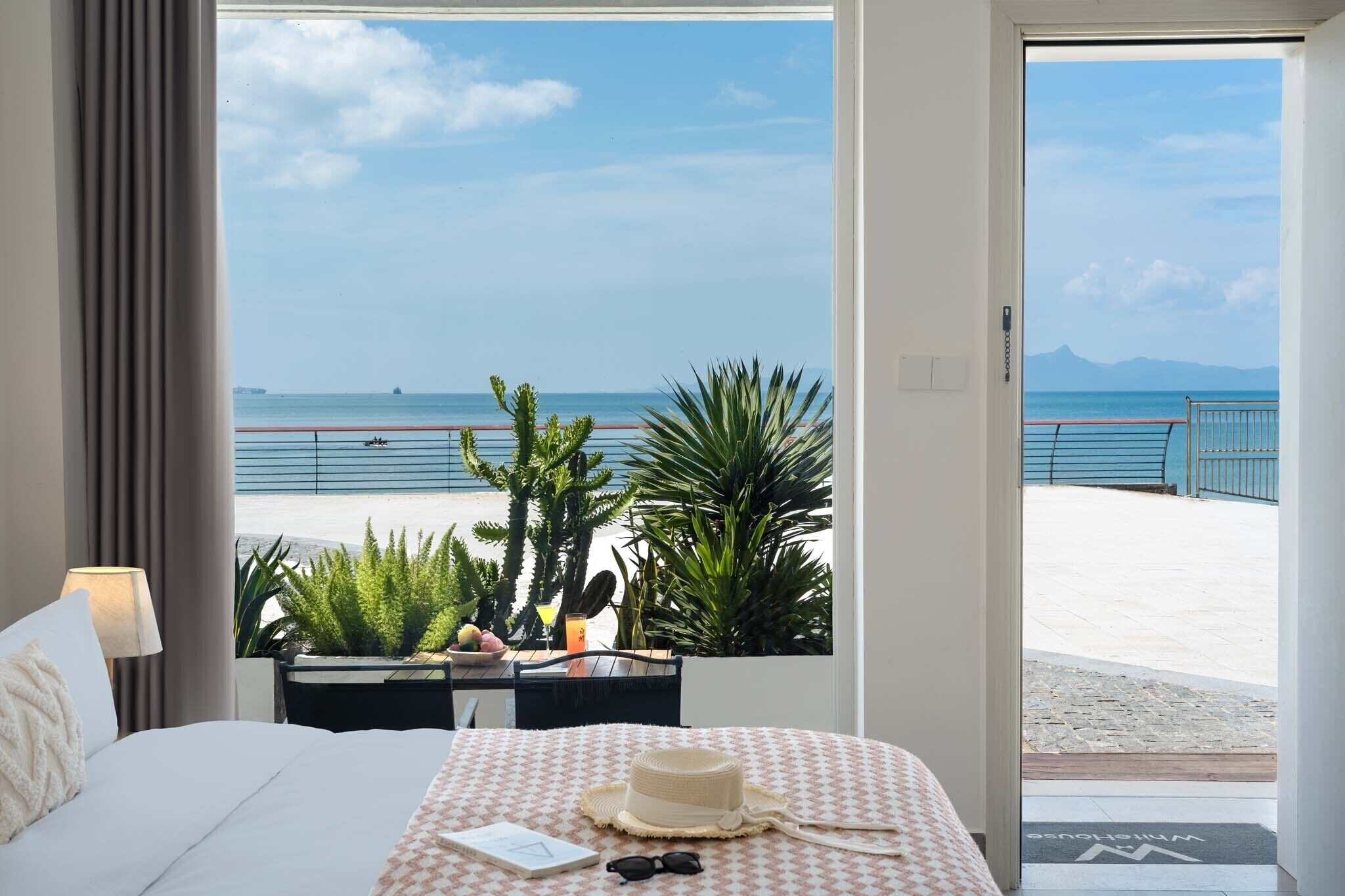 A hotel room with a bed, a desk, and a view of the beach and sea.
