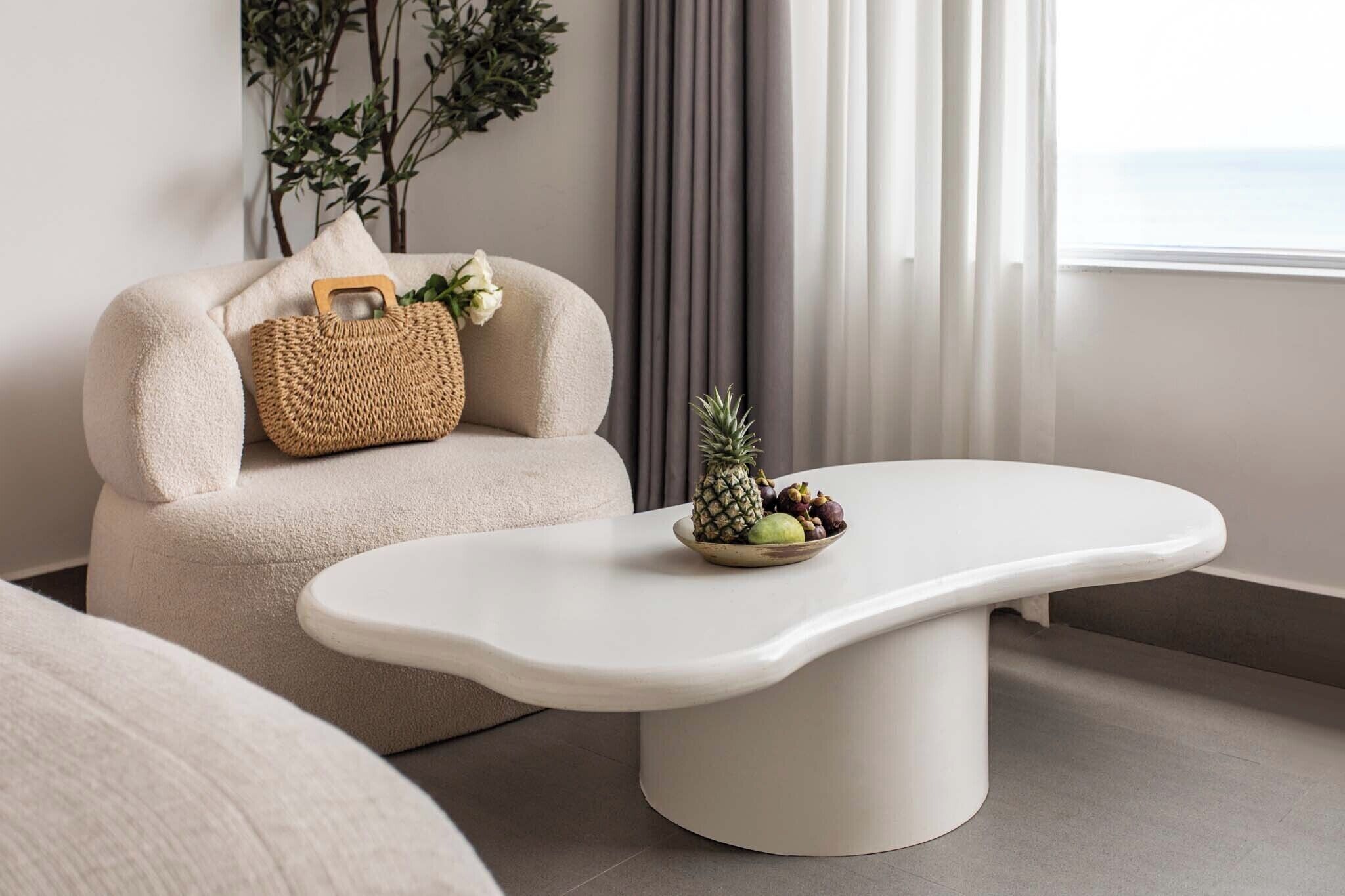 Ein modernes Wohnzimmer mit einem weißen Sofa, einer gewebten Tasche und einer Obstschale auf einem weißen Tisch.