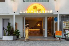 Entrada de un hotel con un cartel con motivos de sol, una recepción y un panel informativo de menú.