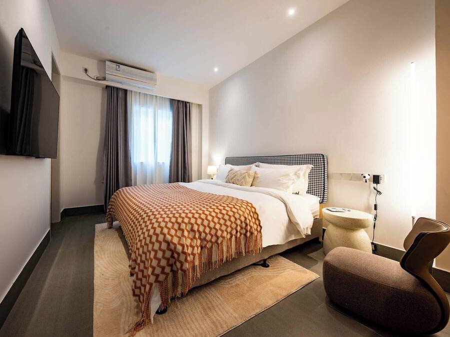 A modern hotel room with a large bed, a flat-screen TV mounted on the wall, a bedside table, and a chair.