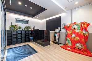 Una habitación de hotel moderna con suelo de madera, un mueble de estanterías negro, un separador de vidrio y un tejido decorativo rojo.