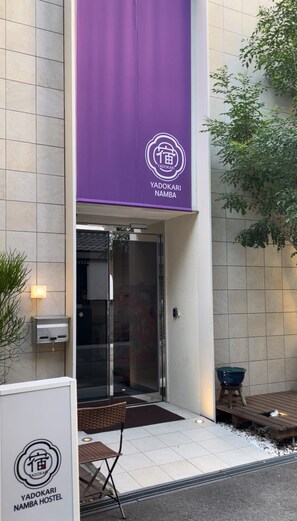 Un edificio con un banderín morado que muestra el logo del Yadokari Namba Hostel.