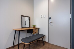 Une pièce comprenant un bureau, un banc, un miroir, une plante fixée au mur et une porte avec une poignée.