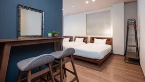 Une chambre d’hôtel avec un bureau, deux lits simples, un miroir et une échelle.
