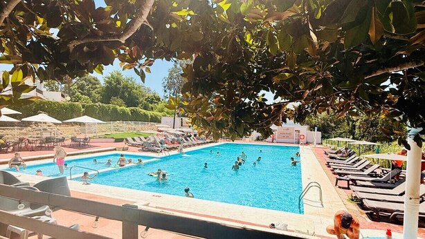 En swimmingpool med mennesker, liggestole og parasoller.