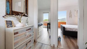 Ein Schlafzimmer mit einem Bett, einem Schminktisch und einem Spiegel. Es gibt einen Balkon mit Blick ins Freie.