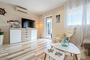 A modern living room with a flat-screen TV, wooden flooring, a white sofa, a dining table with a vase, and a chair. - 01.30 Politur Townhouse with communal pool (Platja d´Aro)
