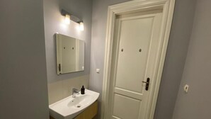 Un baño con lavamanos, espejo y mueble blanco, y una puerta blanca con pomo.