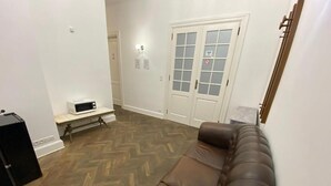 Una sala de estar con un sofá de cuero marrón, una mesita blanca y un microondas en un estante.