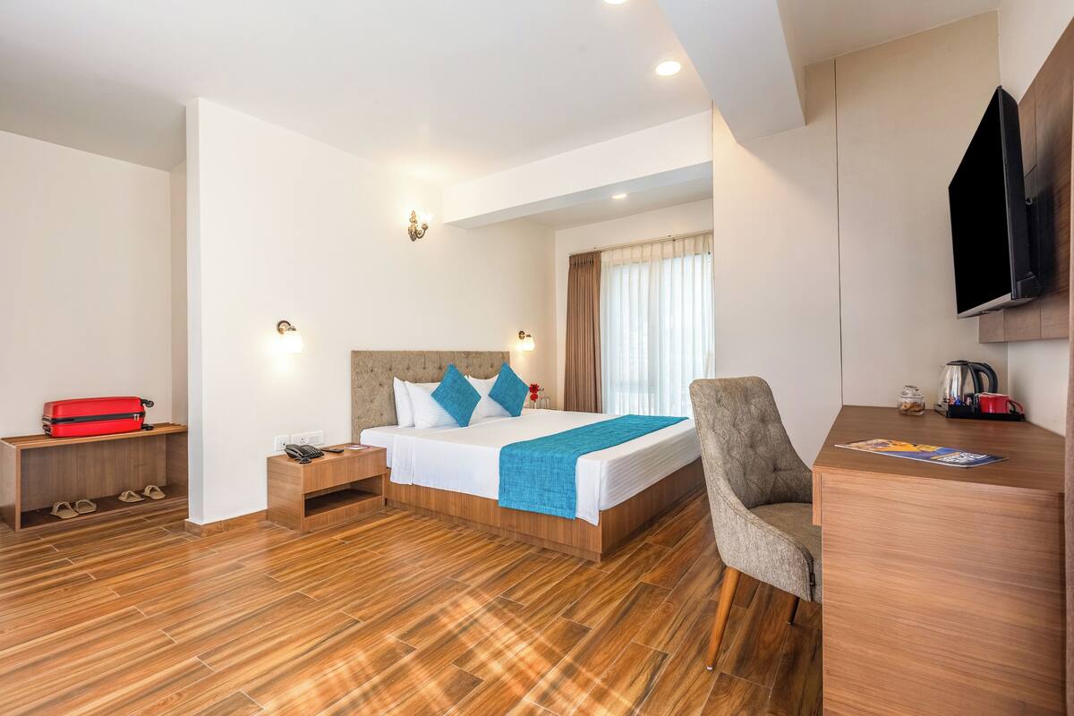 A hotel room with a bed, a desk, a chair, a TV, and a shoe rack.