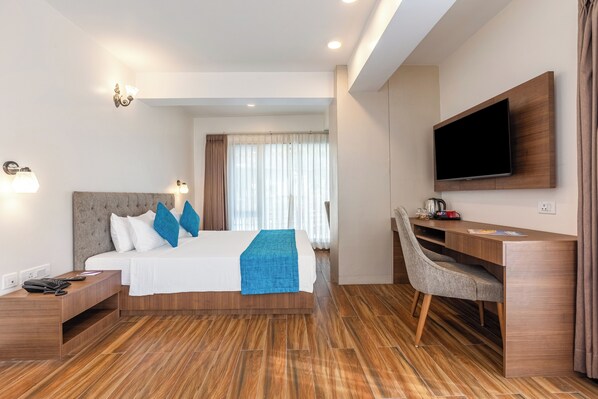 Une chambre d’hôtel moderne dotée d’un grand lit, d’un bureau, d’une télévision à écran plat et d’une fenêtre avec des rideaux.