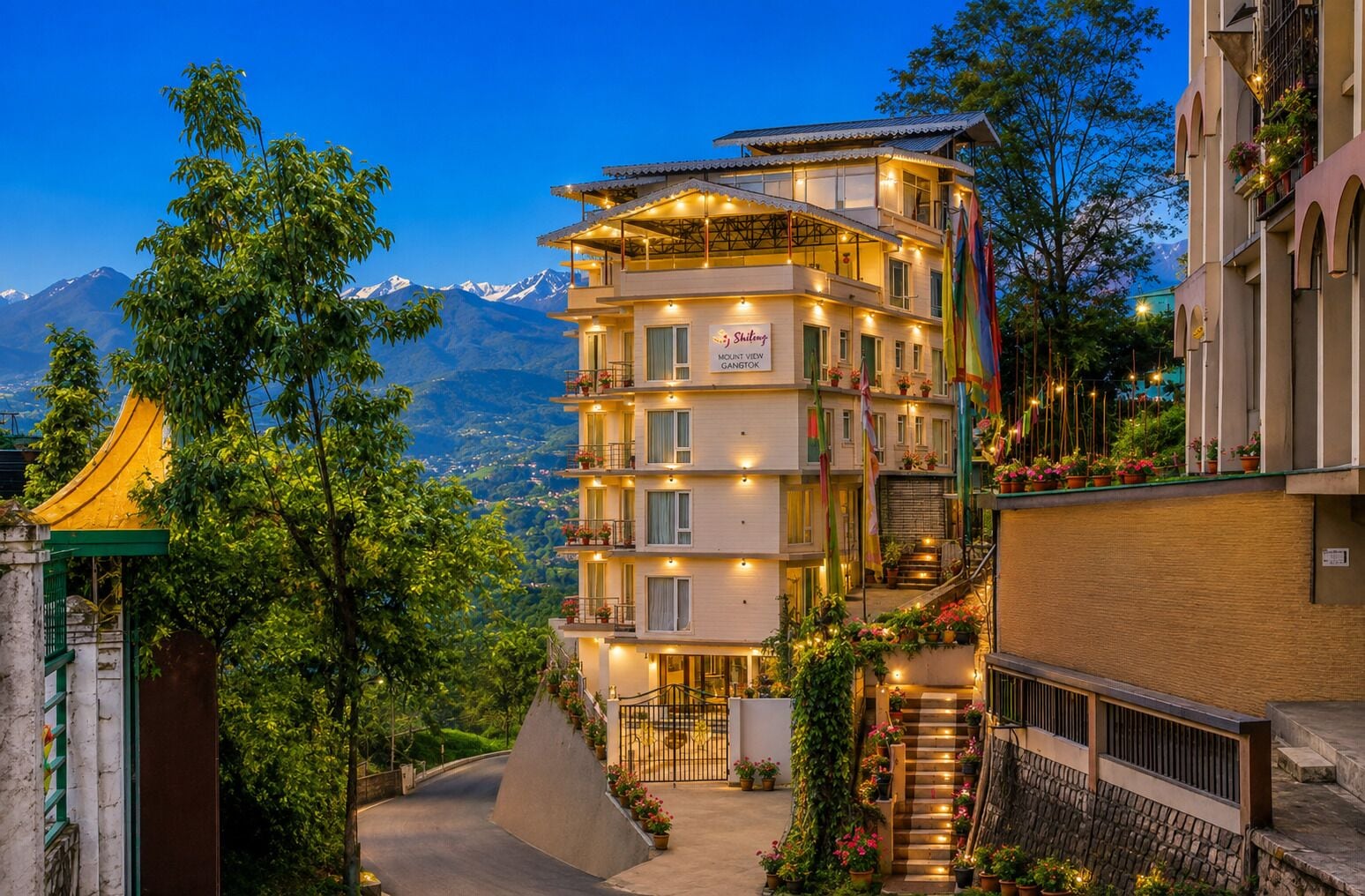 A multi-story hotel with balconies, a staircase, and a view of mountains.