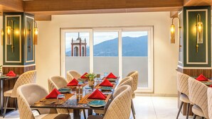 A dining area with a long table set for six, large windows, and a view of a mountain and a building. - Sterling Mount Olive Gangtok (Gangtok)