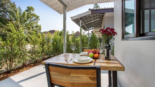 A wooden table set for two with plates, cutlery, a bottle, and a fruit bowl. - Oxavia Garden Bungalow B1-B2 (Rawai)