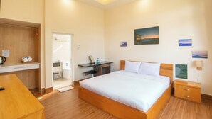 A hotel room with a wooden bed, a desk with a chair, a small table, and a nightstand. - SAVIO Homestay (Lam Vien - Da Lat)