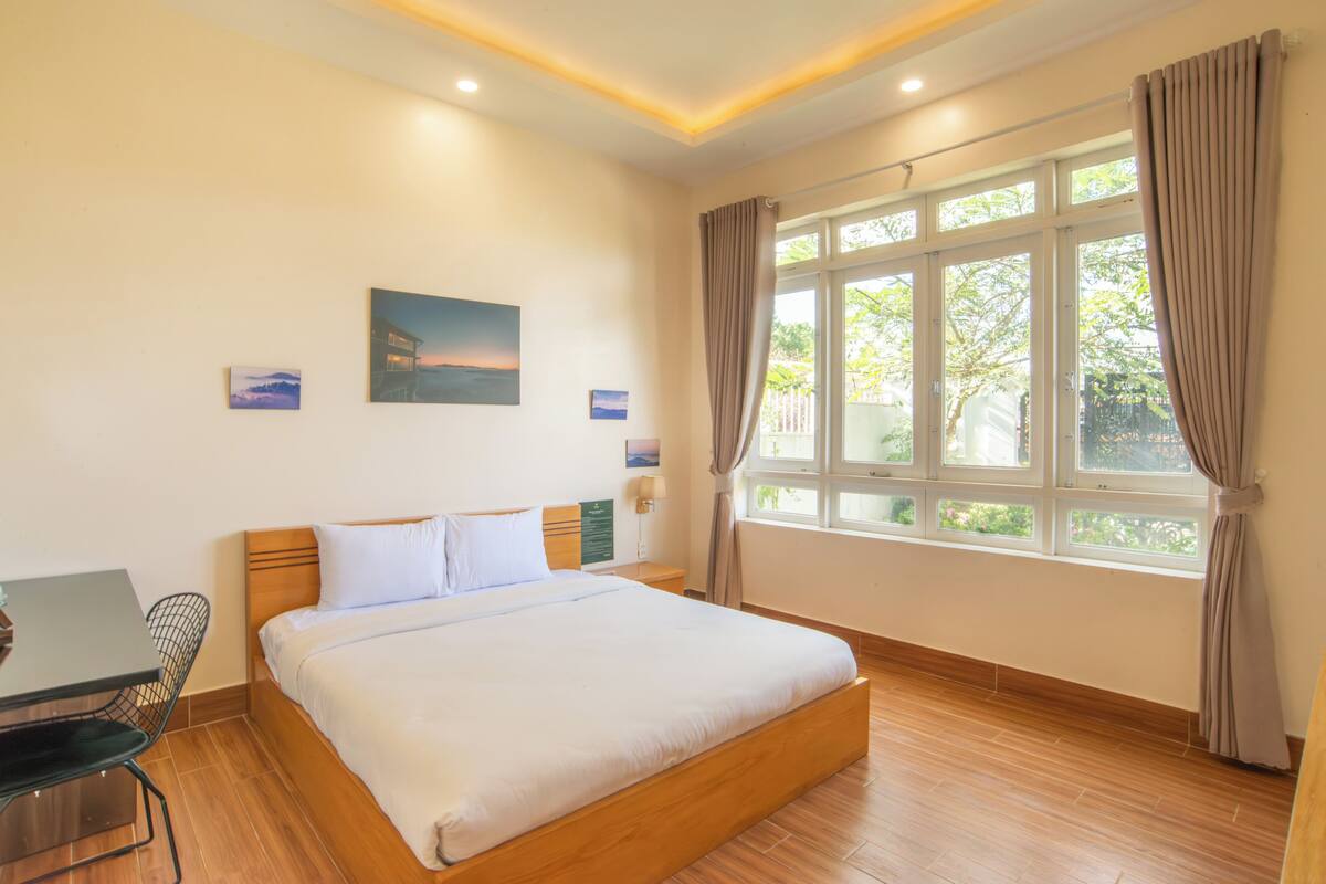 A hotel room with a large bed, a desk, and a window with curtains.