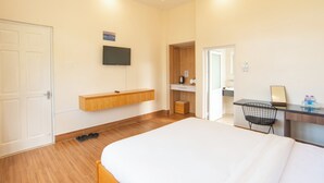 A modern hotel room with a large bed, a wooden bench, a TV mounted on the wall, a desk with a chair, and a small bathroom area. - SAVIO Homestay (Lam Vien - Da Lat)