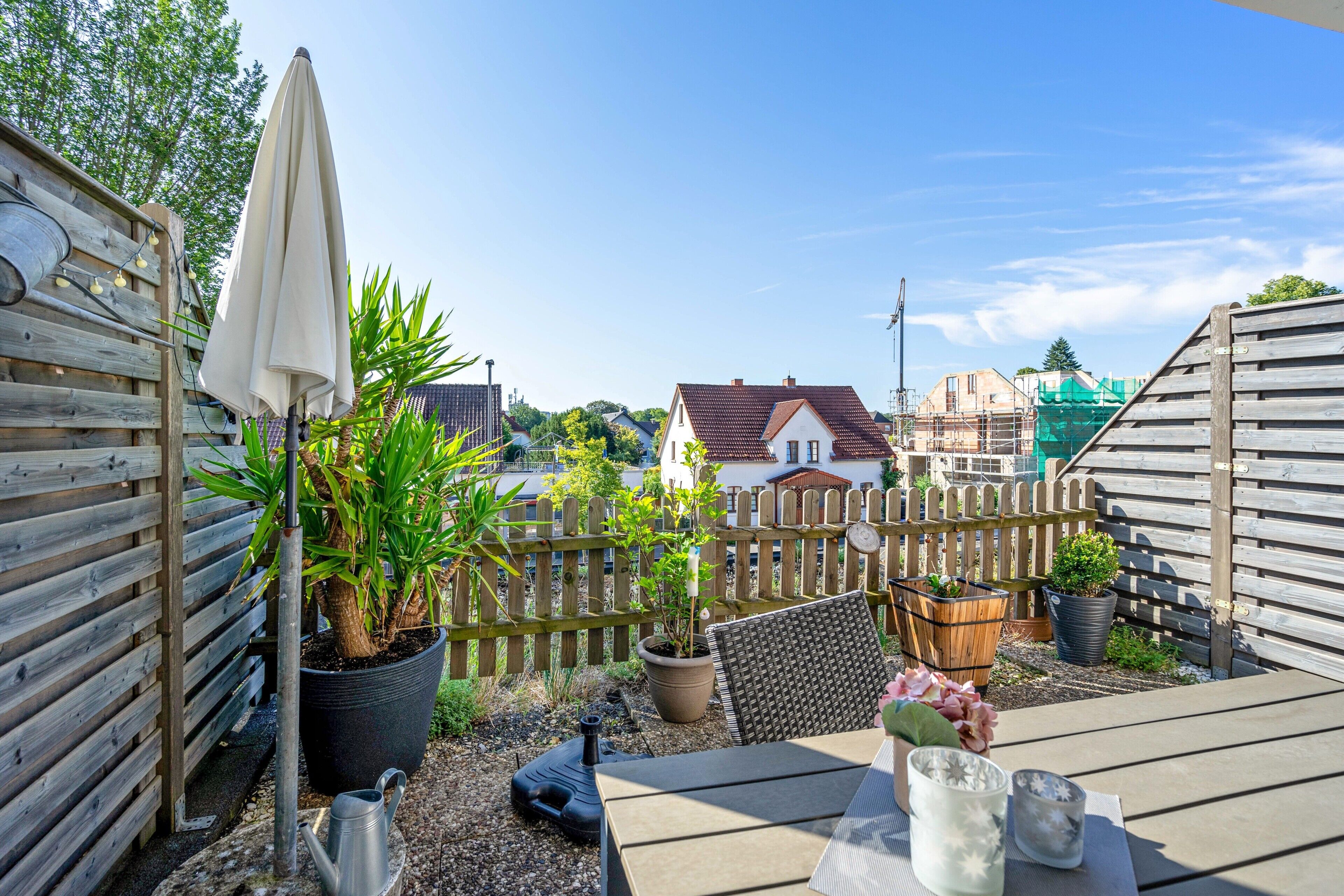 Eine Holzterrasse mit Tisch, Blumentöpfen und einem Metall-Gießkannen.