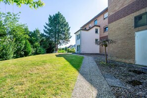 A residential building with a paved driveway, a lawn, and a tree.
