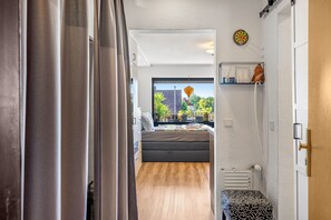 A narrow hallway with a bed and a window, a radiator, and a shelf with items.