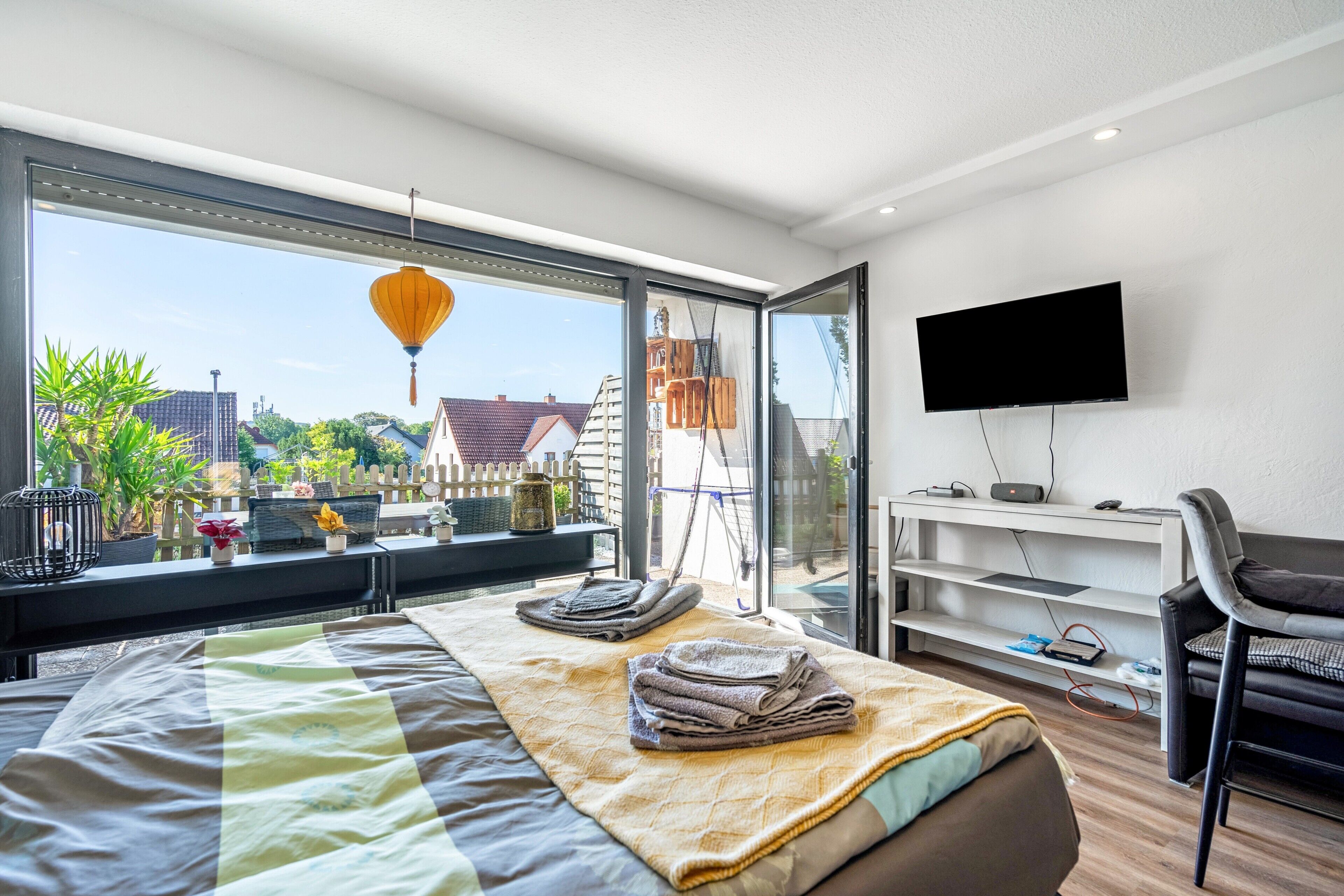 A modern bedroom with a large window, a bed, a TV, and a desk.