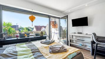 Ein modernes Schlafzimmer mit großem Fenster, einem Bett, einem Fernseher und einem Schreibtisch.