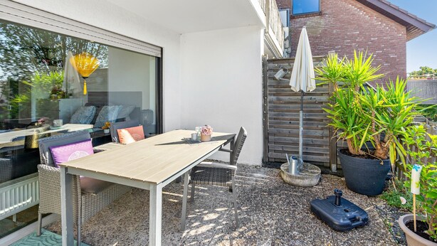 Eine Terrasse im Freien mit Tisch und Stühlen, einem Blumentopf und einem kleinen Garten.