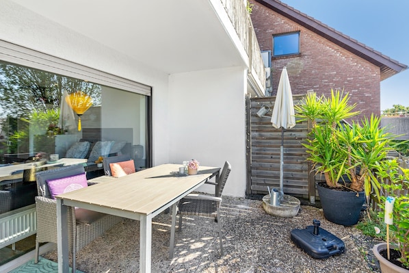 An outdoor patio area with a table and chairs, a potted plant, and a small garden.