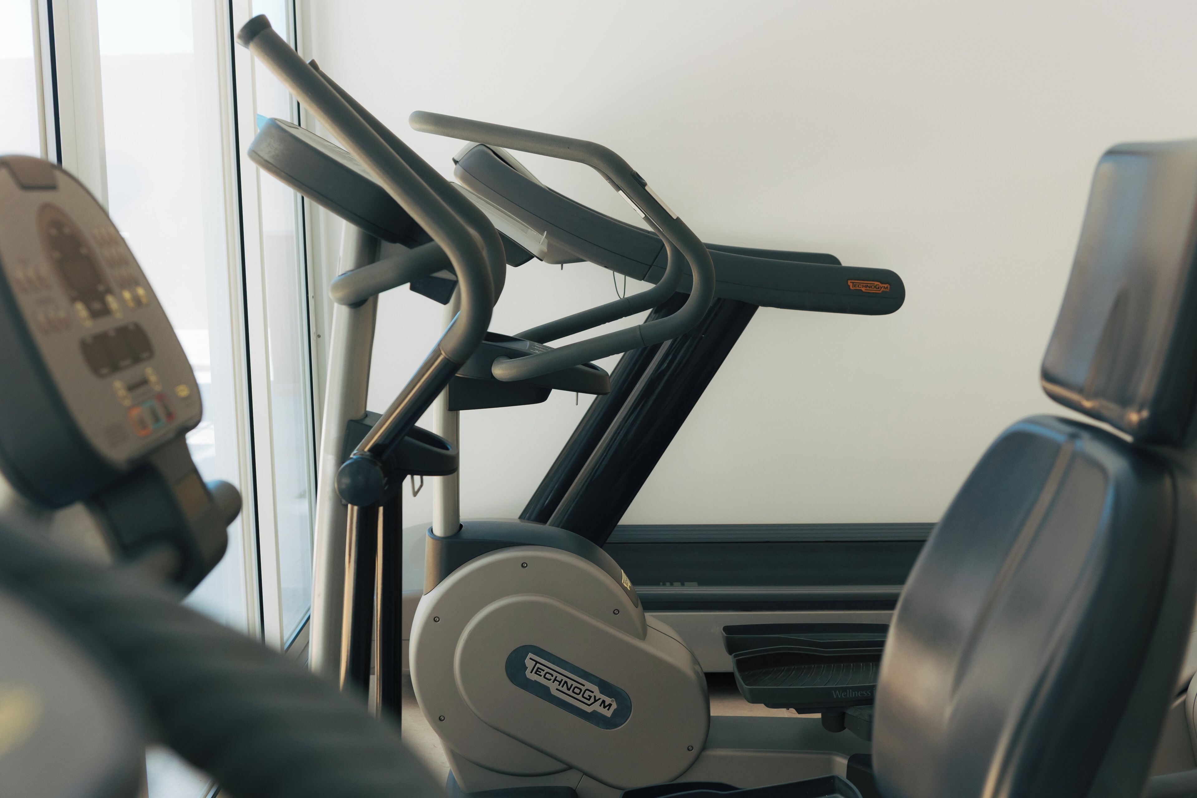 A gym with exercise equipment, including a treadmill and a stationary bike, with a window in the background.