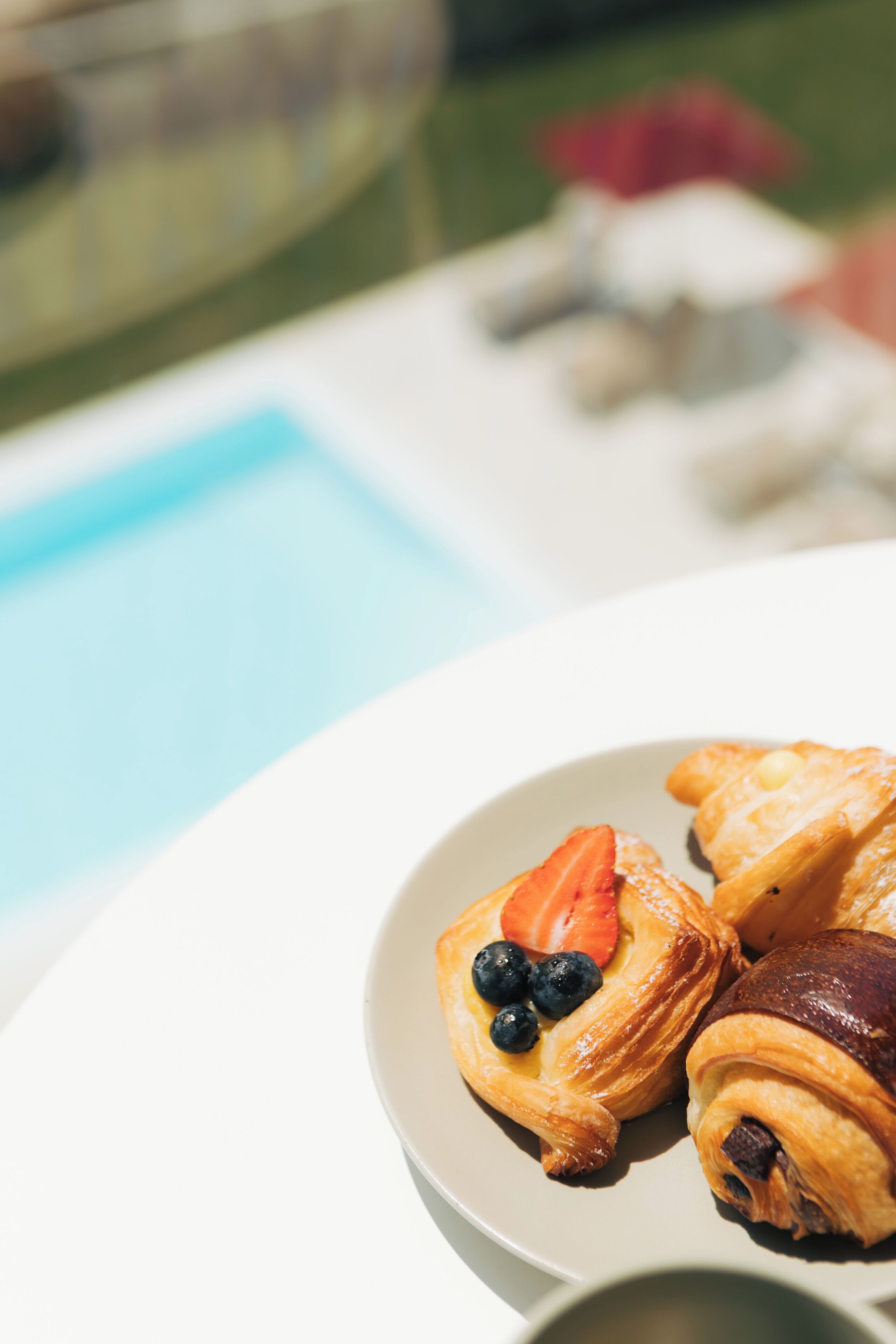 Ein Teller mit Gebäck und Früchten am Poolrand.