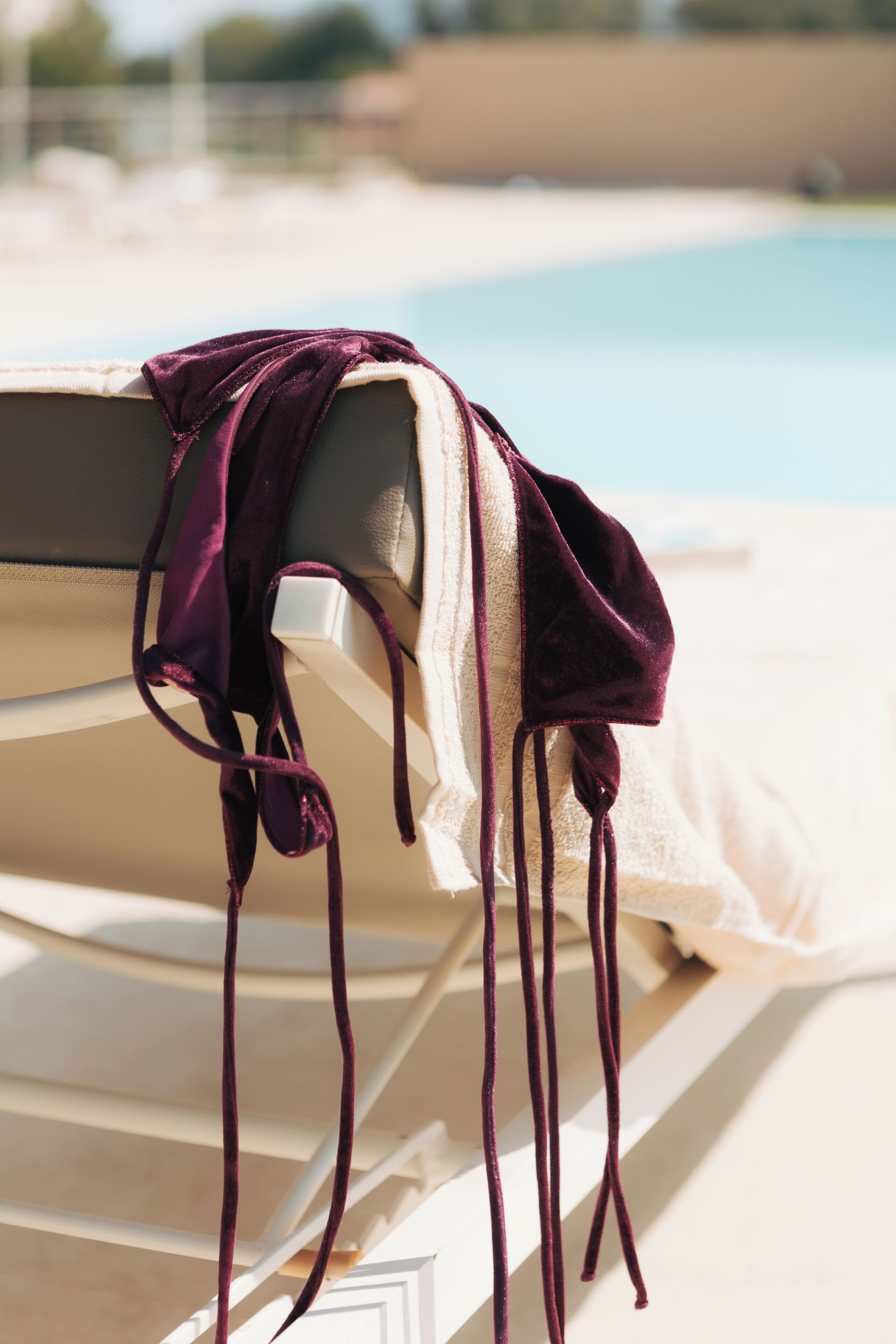 Un fauteuil de relaxation placé au bord de la piscine, doté d’un coussin violet et d’une serviette blanche.