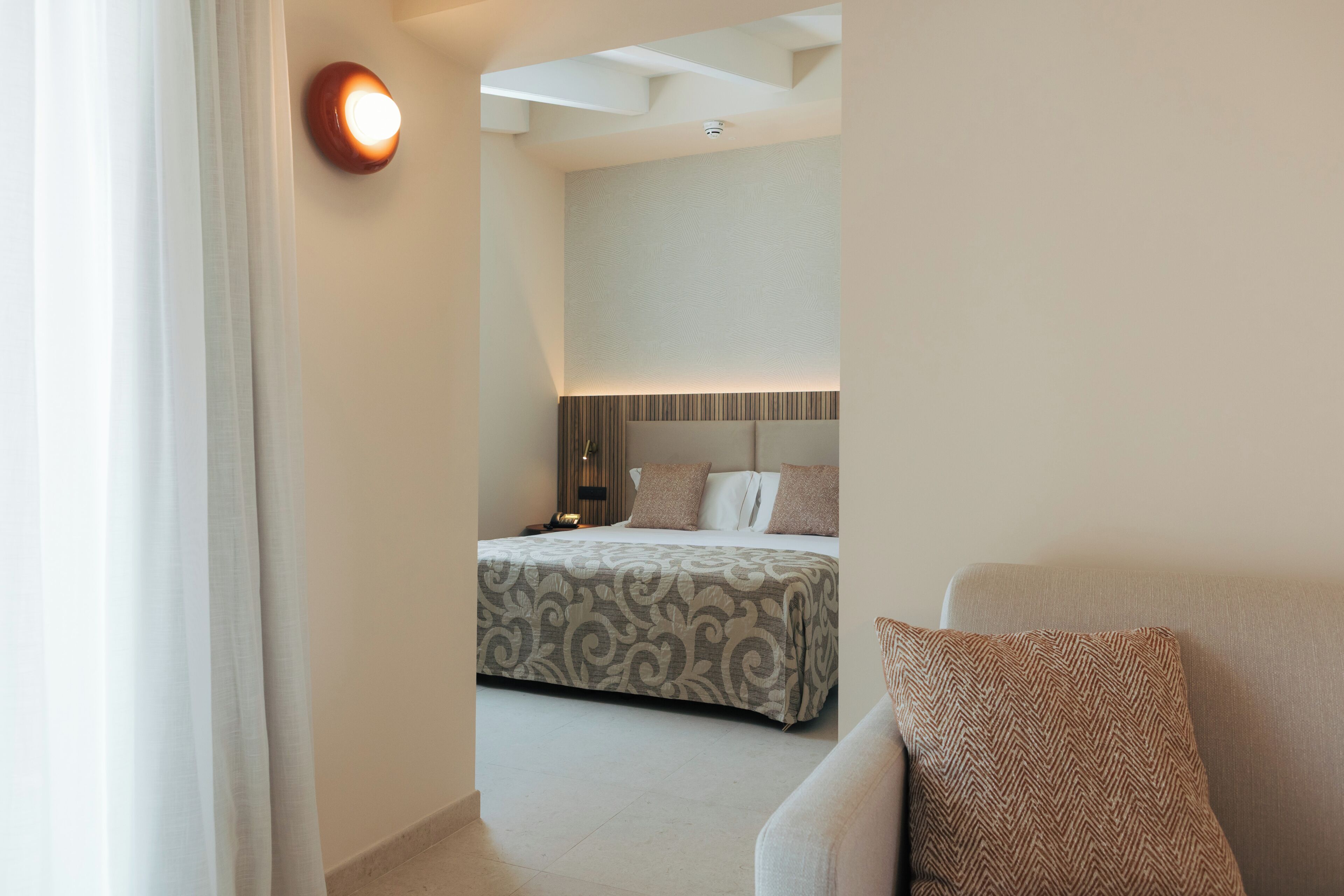 A hotel room with a bed, a bedside table, a lamp, and a sofa.