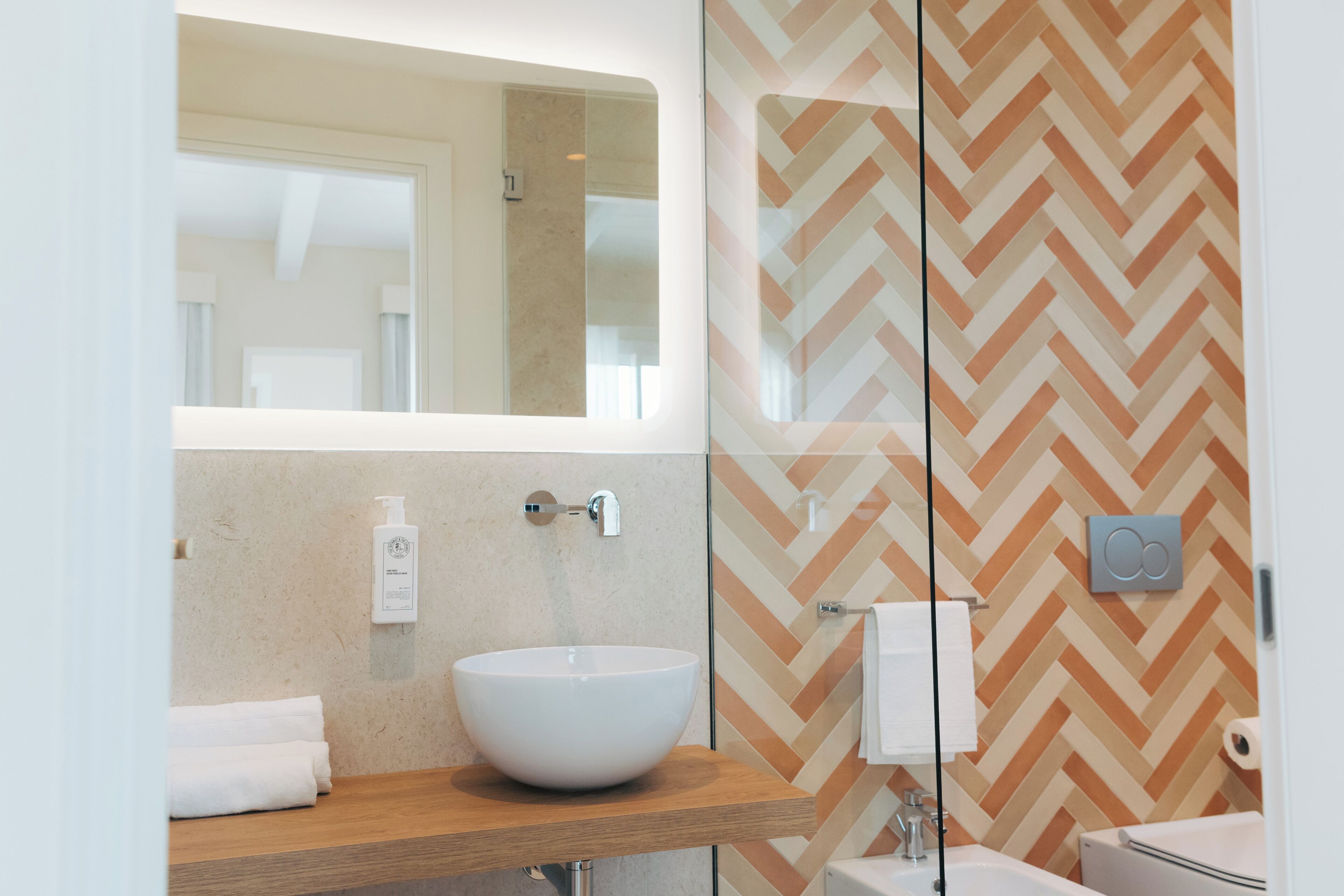 Um banheiro moderno com um espelho grande, pia branca e detalhe na parede em padrão herringbone.