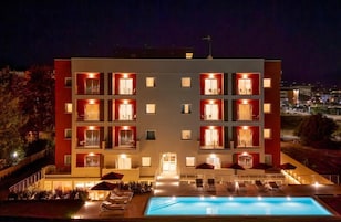 A multi-story hotel with a swimming pool, outdoor seating, and balconies with lights.