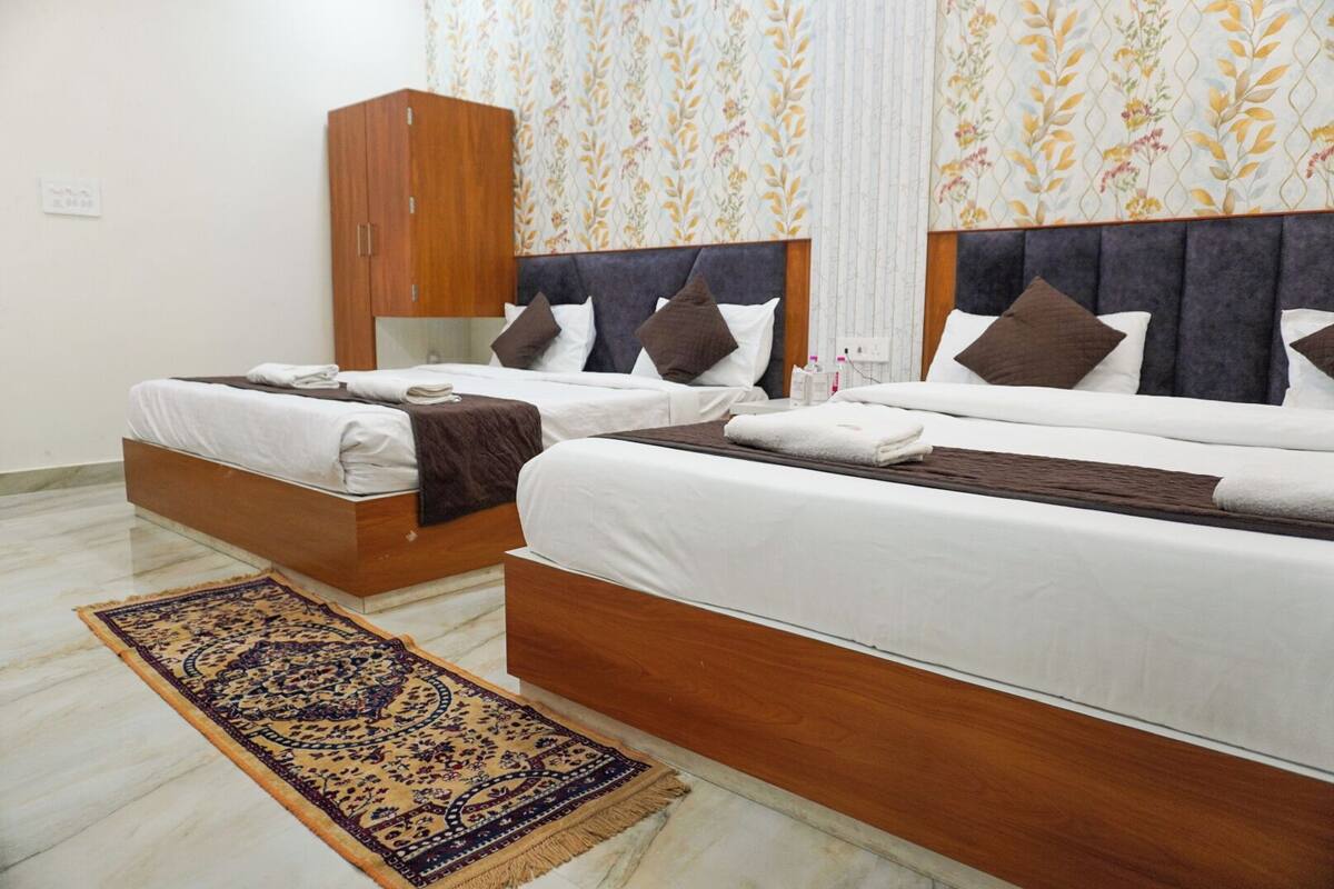 A hotel room with two beds, a wooden wardrobe, a patterned rug, and floral wallpaper.