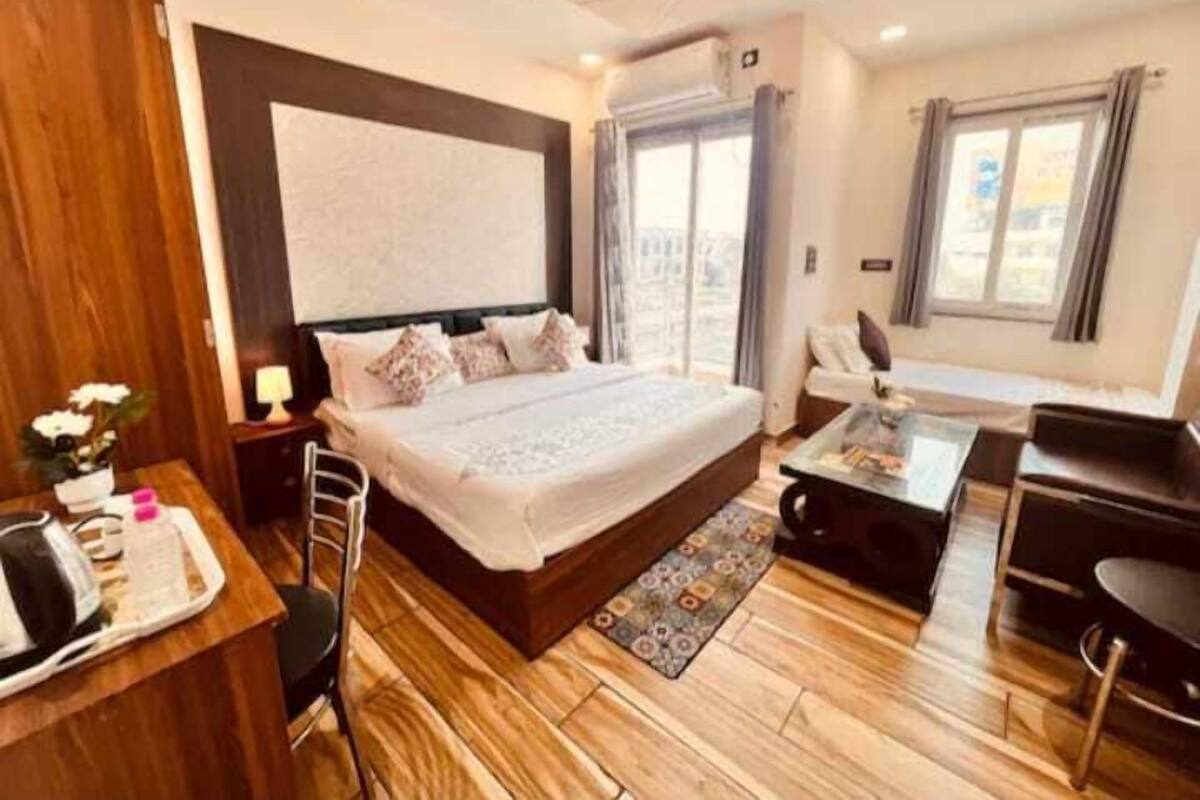 A hotel room with a large bed, a desk with a chair, a small table, and a view of the city through the window.