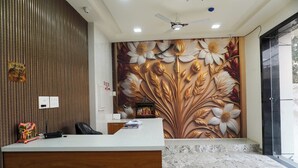 A reception area with a wooden panel wall, a marble floor, a floral mural, and a ceiling fan. - Goyal Hoteliers - Hotel Vasudha (Vrindavan)