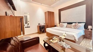A modern bedroom with a large bed, a wooden wardrobe, a leather sofa, and a glass coffee table. - Goyal Hoteliers - Hotel Vasudha (Vrindavan)