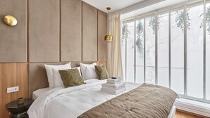 A modern bedroom with a large bed, a wooden headboard, a bedside table with a lamp, and a large window with a view of trees. - Exceptional apartment with AC - Heart of Paris (Paris)