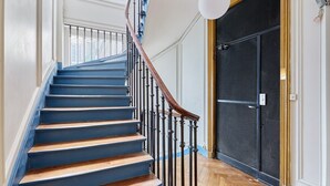A staircase with blue steps and a wooden handrail, leading to a room with a black door and a mesh screen. - Exceptional apartment with AC - Heart of Paris (Paris)