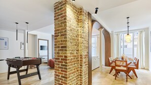 A spacious living room with a brick wall, a foosball table, a dining area with a table and chairs, and a large window providing natural light. - Exceptional apartment with AC - Heart of Paris (Paris)