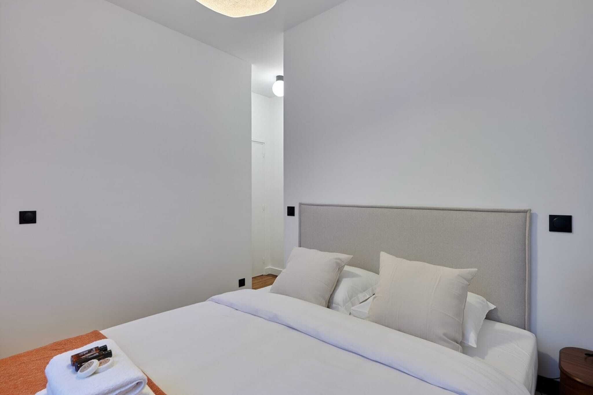 A modern hotel room with a large bed, white linens, and a neutral color scheme.