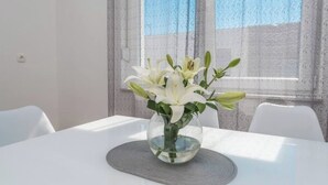 Una mesa con un florero de vidrio transparente que contiene flores blancas, sobre un posavasos con textura.