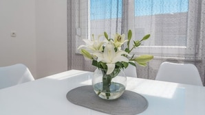 Ett matbord med en genomskinlig glasvas som innehåller vita blommor, placerad på en matta med struktur.