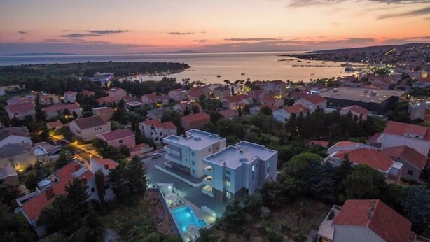 Ett bostadsområde vid kusten med hus, en stor modern byggnad med en swimmingpool och utsikt över havet vid solnedgången.