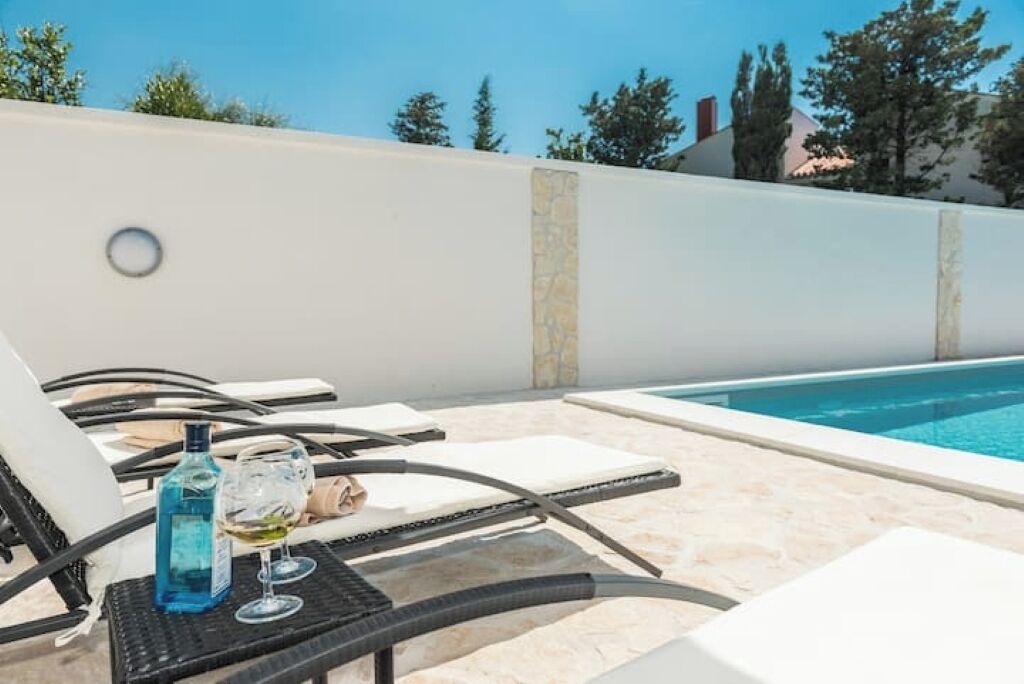 A poolside area with lounge chairs, a table with a bottle and glass, and a clear view of the pool.